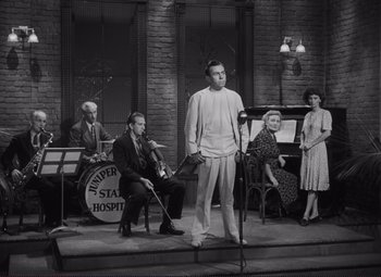 Movie still from “The Snake Pit” (1948), directed by Anatole Litvak – A man standing on a stage in front of a group of people; Wide shot, Low angle