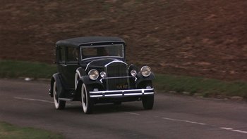 Movie still from “The Song Remains the Same” (1976), directed by Peter Clifton – An old fashioned car driving down a road; Wide shot, High angle