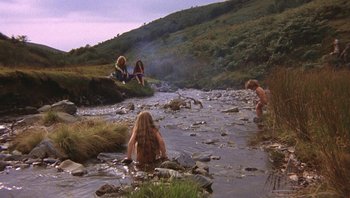 Movie still from “The Song Remains the Same” (1976), directed by Peter Clifton – A group of people sitting and standing in a stream; Wide shot, High angle