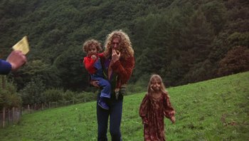 Movie still from “The Song Remains the Same” (1976), directed by Peter Clifton – A woman and two children are standing in a field; Wide shot, High angle