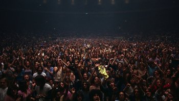 Movie still from “The Song Remains the Same” (1976), directed by Peter Clifton – A large crowd of people in a dark room; Extreme Wide shot, High angle
