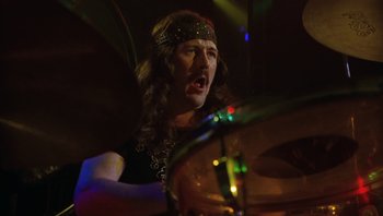 Movie still from “The Song Remains the Same” (1976), directed by Peter Clifton – A man with long brown hair is playing drums; Close Up shot, Low angle