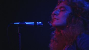 Movie still from “The Song Remains the Same” (1976), directed by Peter Clifton – A man with long red hair and a beard singing into a microphone; Close Up shot, Low angle