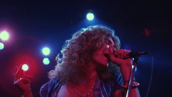 Movie still from “The Song Remains the Same” (1976), directed by Peter Clifton – A woman with curly hair is singing on stage; Medium shot, Low angle