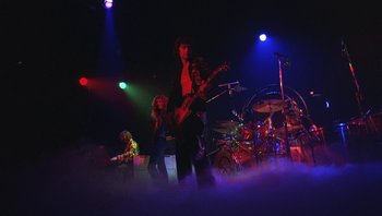 Movie still from “The Song Remains the Same” (1976), directed by Peter Clifton – A group of people that are on a stage; Wide shot, Low angle