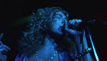 Movie still from “The Song Remains the Same” (1976), directed by Peter Clifton – A man with long hair is singing into a microphone; Close Up shot, Low angle