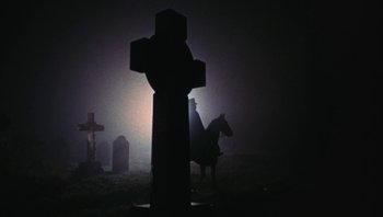 Movie still from “The Song Remains the Same” (1976), directed by Peter Clifton – A cross in the middle of a graveyard at night; Wide shot, Low angle