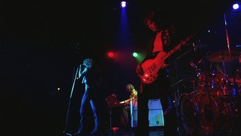Movie still from “The Song Remains the Same” (1976), directed by Peter Clifton – A group of people that are on a stage; Wide shot, Low angle