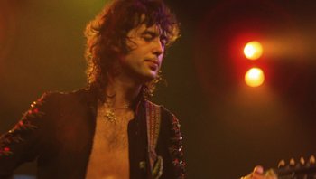 Movie still from “The Song Remains the Same” (1976), directed by Peter Clifton – A person wearing a jacket on a stage; Close Up shot, Low angle