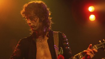 Movie still from “The Song Remains the Same” (1976), directed by Peter Clifton – A person with a guitar on a stage; Close Up shot, Low angle