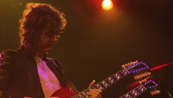 Movie still from “The Song Remains the Same” (1976), directed by Peter Clifton – A man playing a guitar on a stage; Medium shot, Low angle