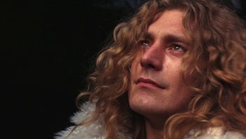 Movie still from “The Song Remains the Same” (1976), directed by Peter Clifton – A person with long curly hair; Close Up shot, Low angle