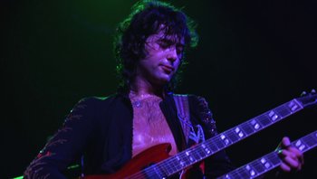 Movie still from “The Song Remains the Same” (1976), directed by Peter Clifton – A man in a black shirt is playing a red guitar; Close Up shot, Low angle
