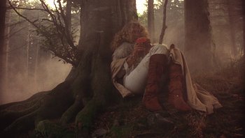 Movie still from “The Song Remains the Same” (1976), directed by Peter Clifton – A woman sitting on the ground next to a tree; Wide shot, Low angle