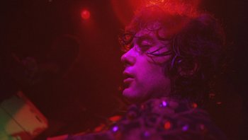 Movie still from “The Song Remains the Same” (1976), directed by Peter Clifton – A man with curly hair is in a purple light; Close Up shot, Low angle