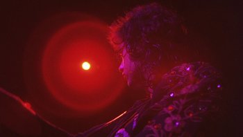 Movie still from “The Song Remains the Same” (1976), directed by Peter Clifton – A person with a red light in the background; Medium shot, Low angle