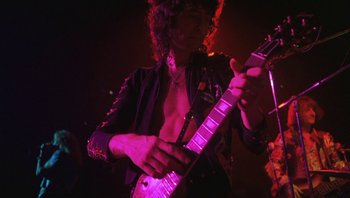 Movie still from “The Song Remains the Same” (1976), directed by Peter Clifton – A person playing a guitar in a dark room; Medium shot, Low angle