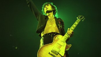 Movie still from “The Song Remains the Same” (1976), directed by Peter Clifton – A man holding a guitar while standing on a stage; Medium shot, Low angle