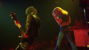Movie still from “The Song Remains the Same” (1976), directed by Peter Clifton – A couple of people that are on a stage together; Wide shot, Low angle