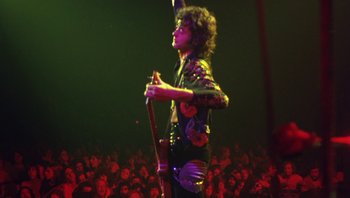 Movie still from “The Song Remains the Same” (1976), directed by Peter Clifton – A man with a guitar in front of an audience; Medium shot, Low angle