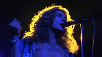 Movie still from “The Song Remains the Same” (1976), directed by Peter Clifton – A person with long hair on a stage; Close Up shot, Low angle