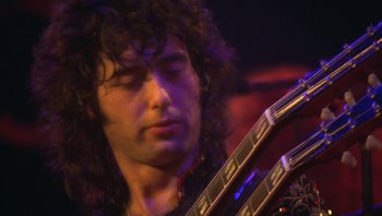 Movie still from “The Song Remains the Same” (1976), directed by Peter Clifton – A person holding a guitar; Close Up shot, Low angle
