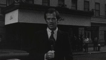 Movie still from “The Song Remains the Same” (1976), directed by Peter Clifton – A black and white photo of a man holding a microphone; Medium shot, Low angle