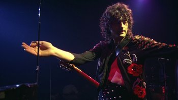 Movie still from “The Song Remains the Same” (1976), directed by Peter Clifton – A man holding a guitar in his hand; Medium shot, Low angle