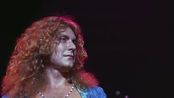 Movie still from “The Song Remains the Same” (1976), directed by Peter Clifton – A person with long curly hair; Close Up shot, Low angle