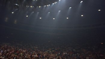 Movie still from “The Song Remains the Same” (1976), directed by Peter Clifton – A crowd of people in an arena lit up by spotlights; Extreme Wide shot, Low angle