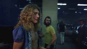 Movie still from “The Song Remains the Same” (1976), directed by Peter Clifton – A man with long blonde hair standing next to another man with a beard; Medium shot, Low angle