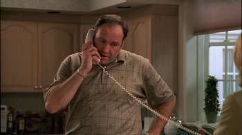 Movie still from “The Sopranos” (1999), created by David Chase – A man talking on a phone while standing in a kitchen; Medium shot, Low angle