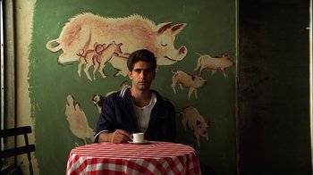 Movie still from “The Sopranos” (1999), created by David Chase – A man sitting at a table drinking a cup of coffee; Medium shot, Low angle
