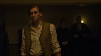 Movie still from “Anne with an E” (2017), created by Moira Walley-Beckett – A man standing in a dimly - lit room next to two other men; Medium shot, Low angle