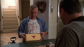 Movie still from “The Sopranos” (1999), created by David Chase – A man holding a box in front of another man at a table; Medium shot, Low angle