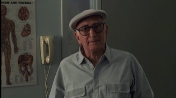 Movie still from “The Sopranos” (1999), created by David Chase – An older man wearing glasses and a hat is standing in front of a phone; Close Up shot, Low angle