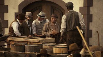 Movie still from “Anne with an E” (2017), created by Moira Walley-Beckett – A group of men standing next to each other in front of barrels; Medium shot, Over the shoulder angle