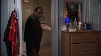 Movie still from “The Sopranos” (1999), created by David Chase – A man standing in a living room holding a pizza; Medium shot, High angle