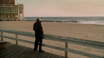Movie still from “The Sopranos” (1999), created by David Chase – A man standing on a boardwalk looking out at the ocean; Wide shot, High angle