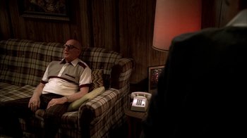 Movie still from “The Sopranos” (1999), created by David Chase – An older man sitting on a chair in a living room; Medium shot, Over the shoulder angle