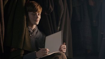 Movie still from “Anne with an E” (2017), created by Moira Walley-Beckett – A young man sitting in a chair holding a laptop; Medium shot, Overhead angle
