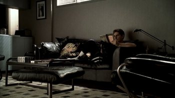 Movie still from “The Sopranos” (1999), created by David Chase – A man sitting on top of a couch reading a book; Wide shot, High angle