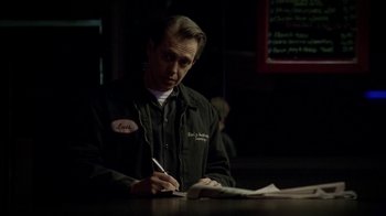 Movie still from “The Sopranos” (1999), created by David Chase – A man sitting at a table writing on a piece of paper; Medium shot, Over the shoulder angle
