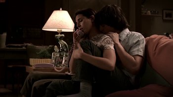 Movie still from “The Sopranos” (1999), created by David Chase – A man and a woman sitting on a couch holding a phone; Medium shot, High angle