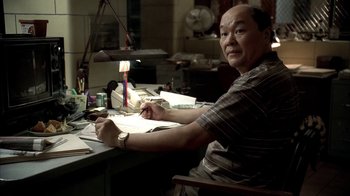 Movie still from “The Sopranos” (1999), created by David Chase – A man sitting at a desk writing on a piece of paper; Medium shot, High angle