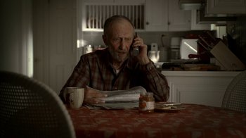 Movie still from “The Sopranos” (1999), created by David Chase – An older man sitting at a table talking on a phone; Medium shot, High angle