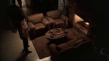 Movie still from “The Sopranos” (1999), created by David Chase – A man standing in front of a fireplace in a living room; Wide shot, High angle