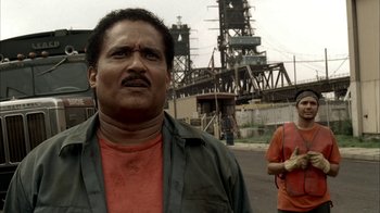 Movie still from “The Sopranos” (1999), created by David Chase – A man standing on the side of a road near a bridge; Medium shot, Low angle