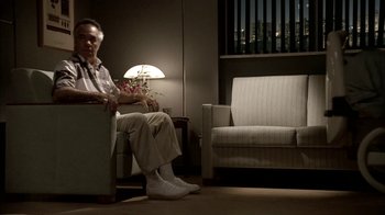 Movie still from “The Sopranos” (1999), created by David Chase – An older man sitting in a chair in a room; Wide shot, Low angle