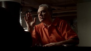 Movie still from “The Sopranos” (1999), created by David Chase – An older man in an orange shirt is sitting at a table; Medium shot, Low angle